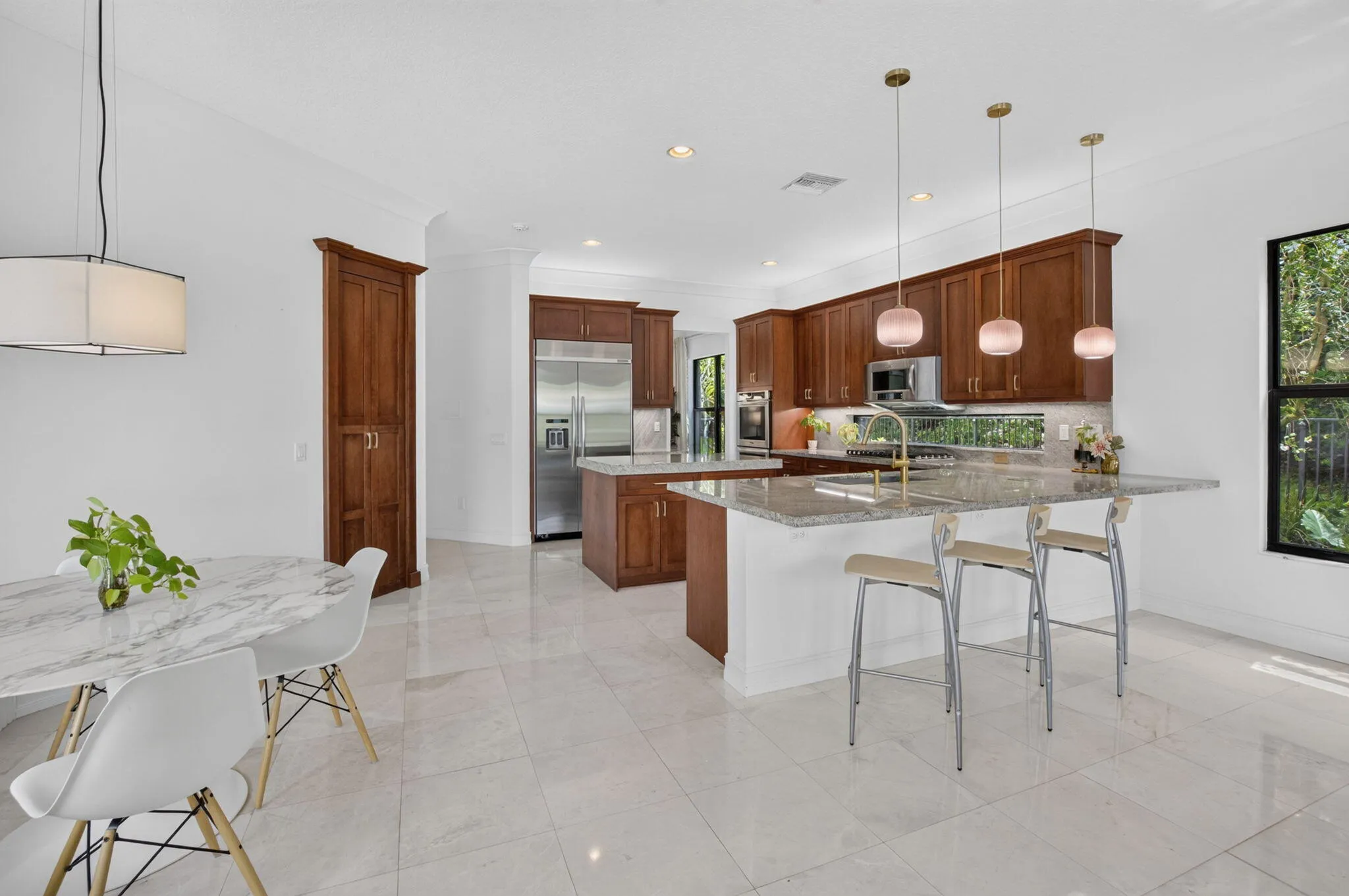 Spacious kitchen featuring warm wood cabinetry, stainless steel appliances, a multi-level island with seating, a window backsplash, and pendant lighting