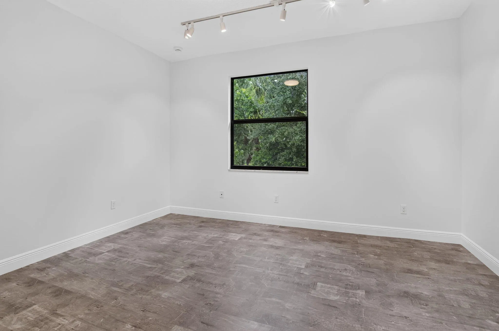 Spacious room featuring wood-finish flooring, white walls, and a black-framed window