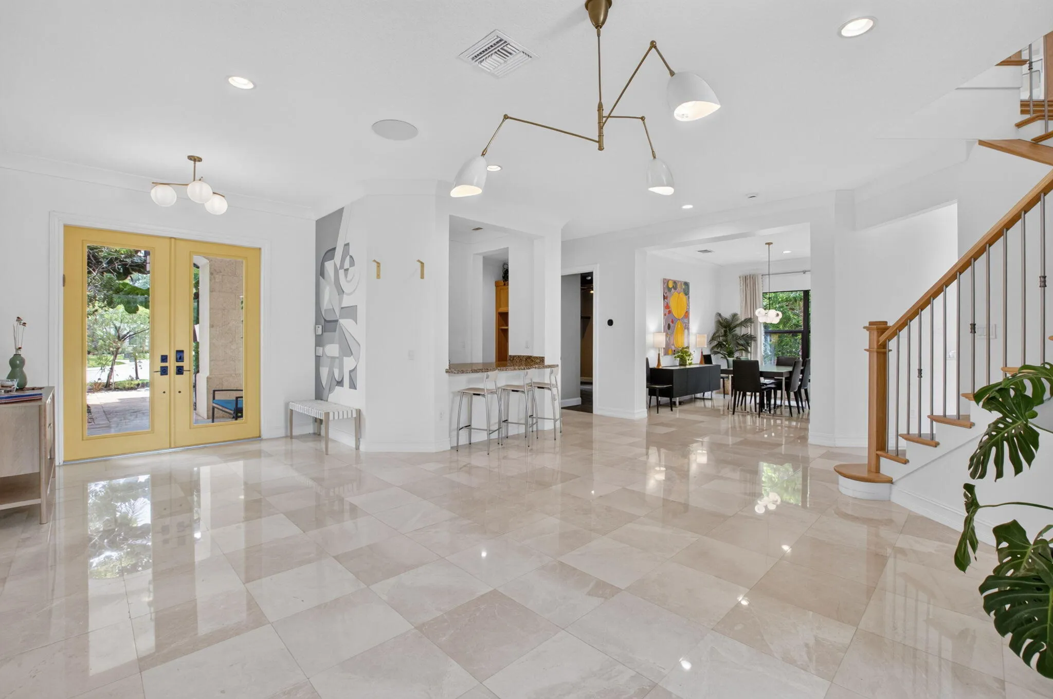 Spacious entry foyer featuring large format tile flooring, a prominent staircase with wood newel posts and metal balusters, and a contemporary chandelier