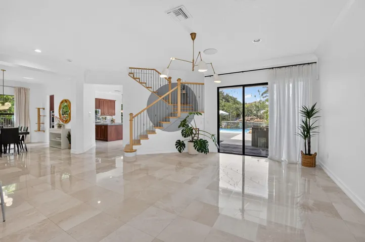 Expansive main living area featuring polished tile flooring, a contemporary chandelier, a staircase with wood newel posts and metal spindles, and large sliding glass doors opening to a pool area