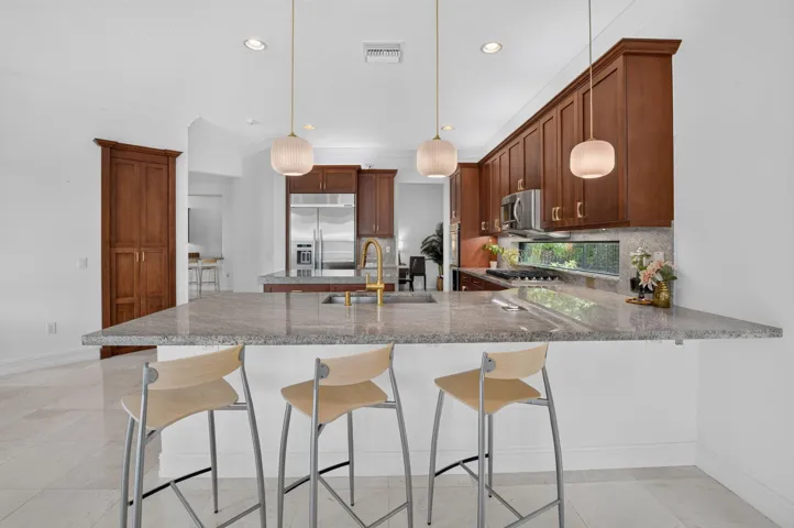Kitchen featuring an expansive island with a light-toned countertop, warm wood-finish cabinetry, stainless steel appliances, and under-cabinet lighting