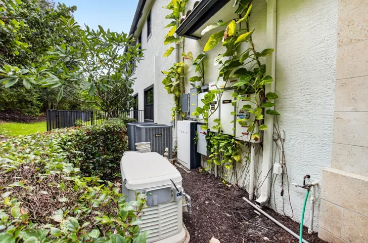 Exterior utility area featuring a standby generator, multiple electrical panels, and air conditioning units