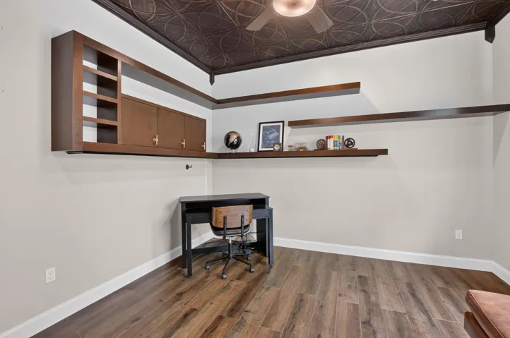 Room featuring wood-finish flooring, a decorative patterned ceiling, and a ceiling fan