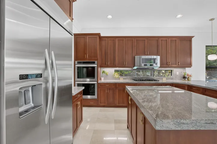 Gourmet kitchen featuring a stainless steel side-by-side refrigerator, double wall ovens, a gas range with a contemporary hood, wood cabinetry, and stone countertops
