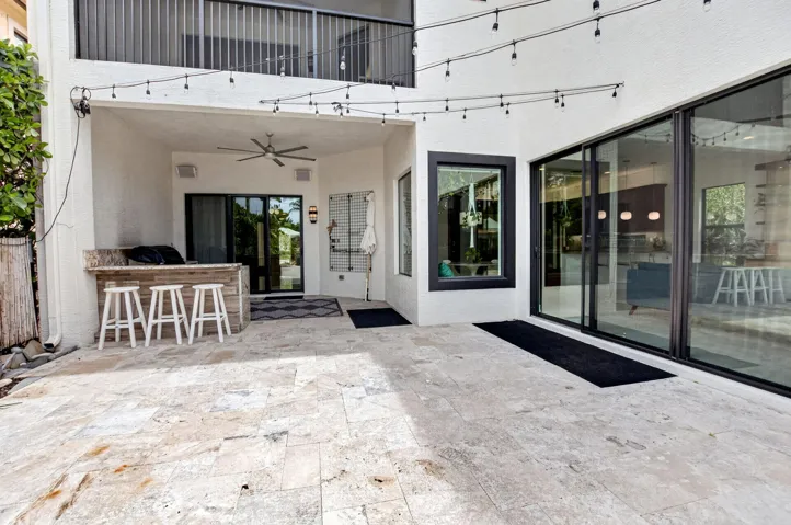 Spacious outdoor patio featuring natural stone flooring, an integrated outdoor bar with a stone countertop, a ceiling fan, and large sliding glass doors providing access to the interior