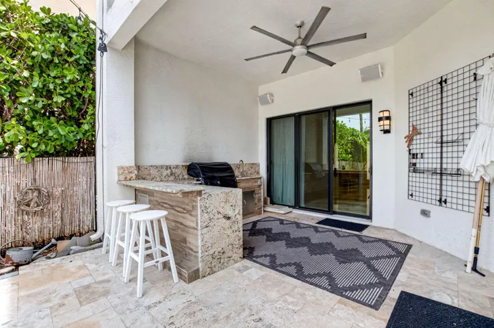 Covered outdoor patio featuring a built-in outdoor kitchen with stone-finish countertops, a ceiling fan, and sliding glass doors