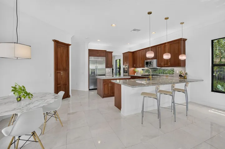 Spacious kitchen featuring warm wood cabinetry, stainless steel appliances, a multi-level island with seating, a window backsplash, and pendant lighting
