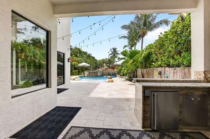 Outdoor living area featuring a built-in outdoor kitchen with stainless steel appliances, a spacious paved patio, and a swimming pool with a rock waterfall