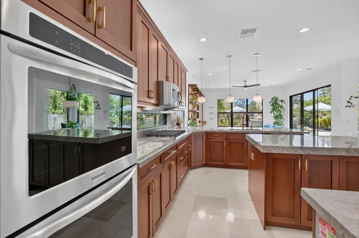 Gourmet kitchen featuring stainless steel double ovens, rich wood cabinetry with gold-tone hardware, light-toned stone countertops, and recessed lighting