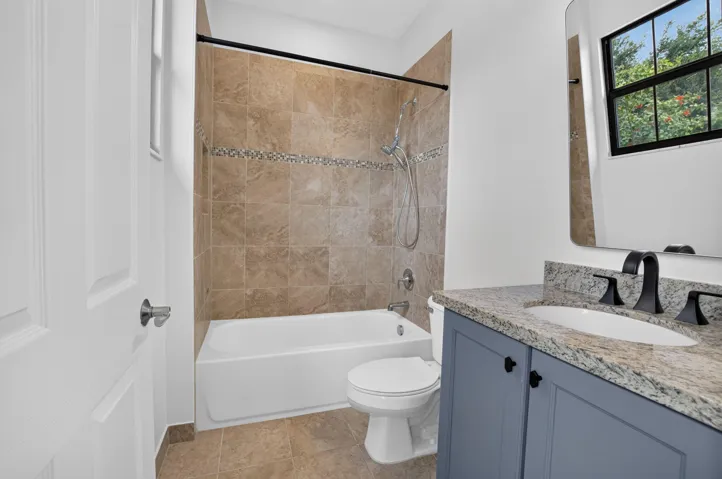 Bathroom featuring a tub/shower combination with tile surround and decorative accent band, a single vanity with granite countertop and undermount sink, and a framed mirror
