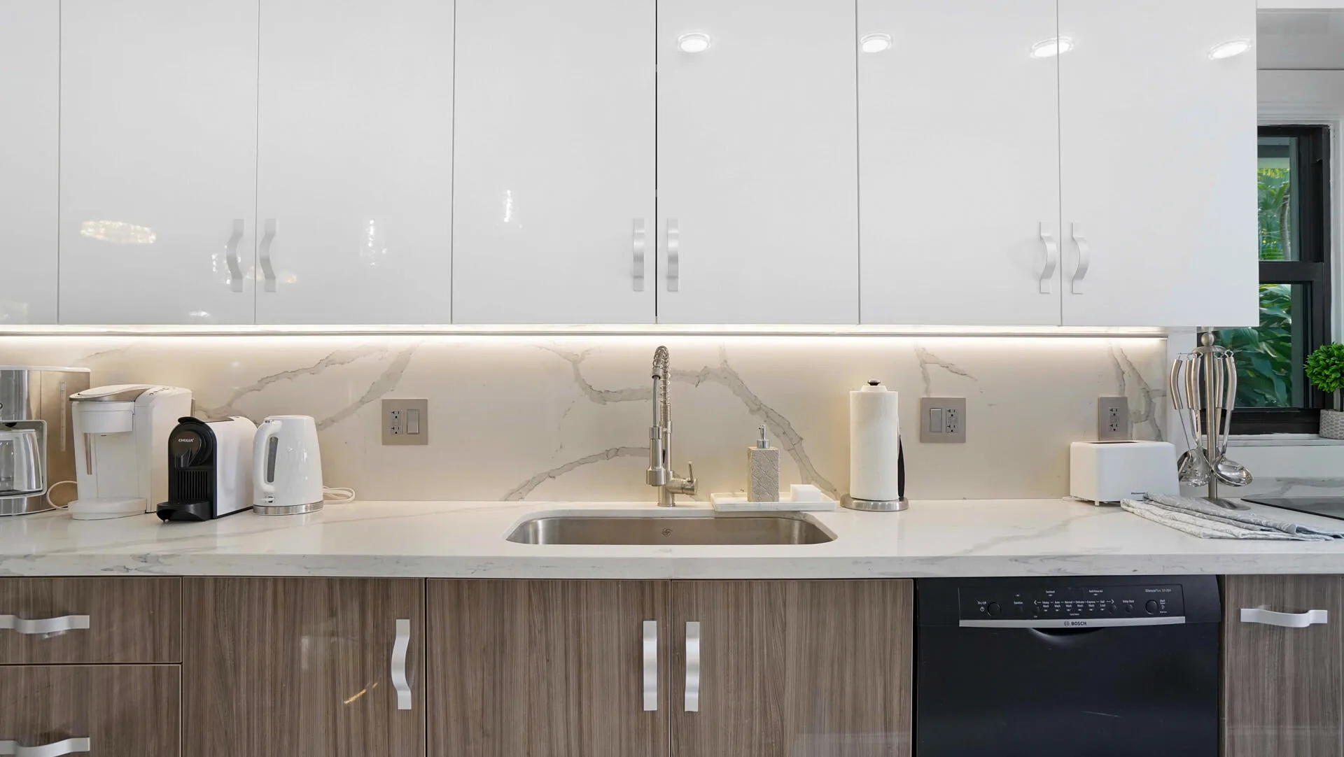 Modern kitchen featuring white glossy upper cabinetry and wood-finish lower cabinetry, complemented by a stone countertop and matching full-height backsplash
