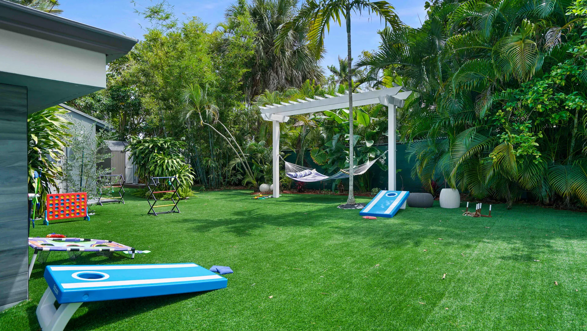 Manicured green lawn featuring a white pergola, lush tropical foliage, and mature palm trees