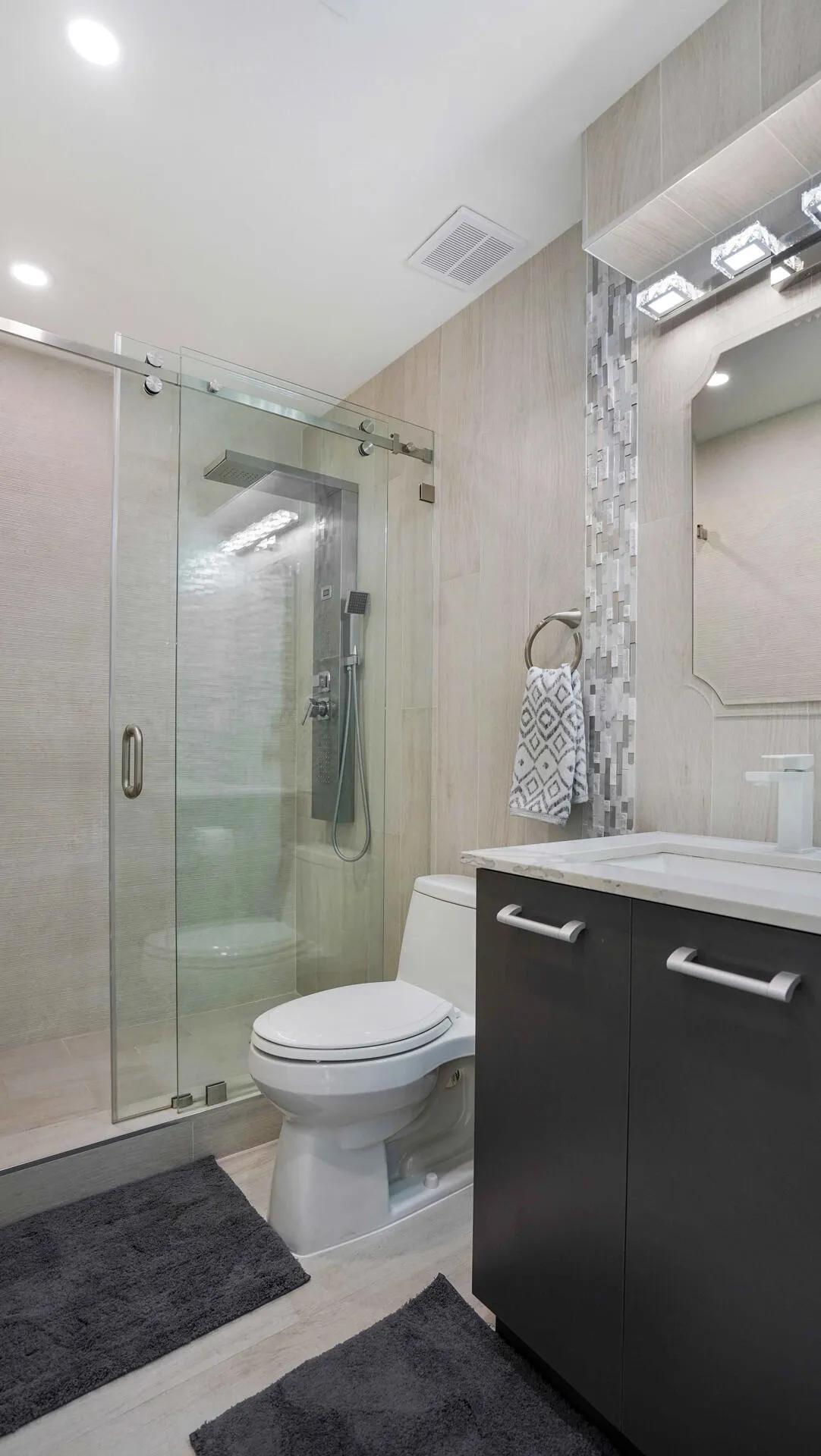 Contemporary bathroom featuring a frameless glass shower enclosure, a dark vanity with a white countertop and integrated sink, and light-toned wall tiling