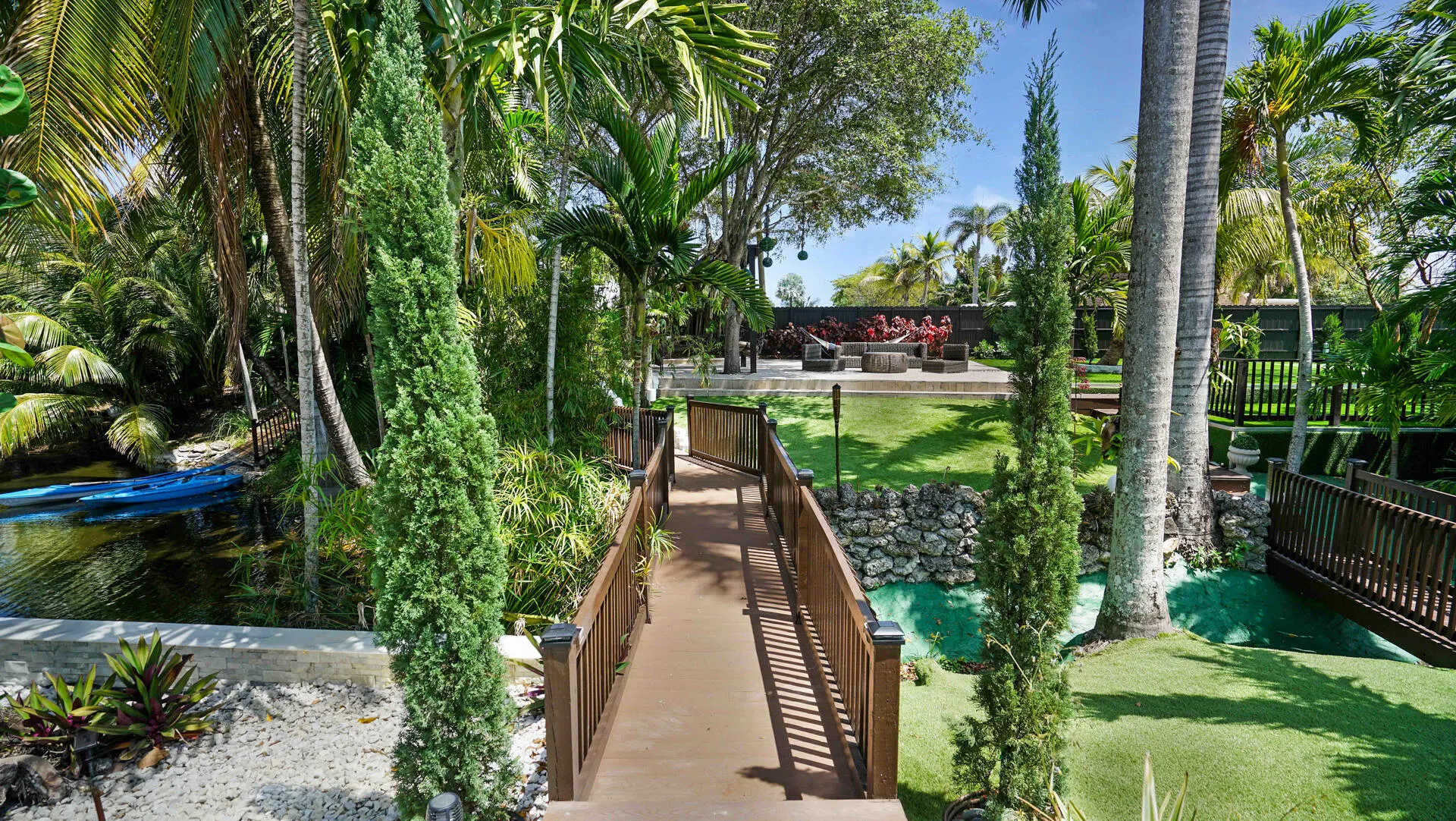 Expansive tropical landscaping featuring a wooden walkway, lush greenery, and a water feature