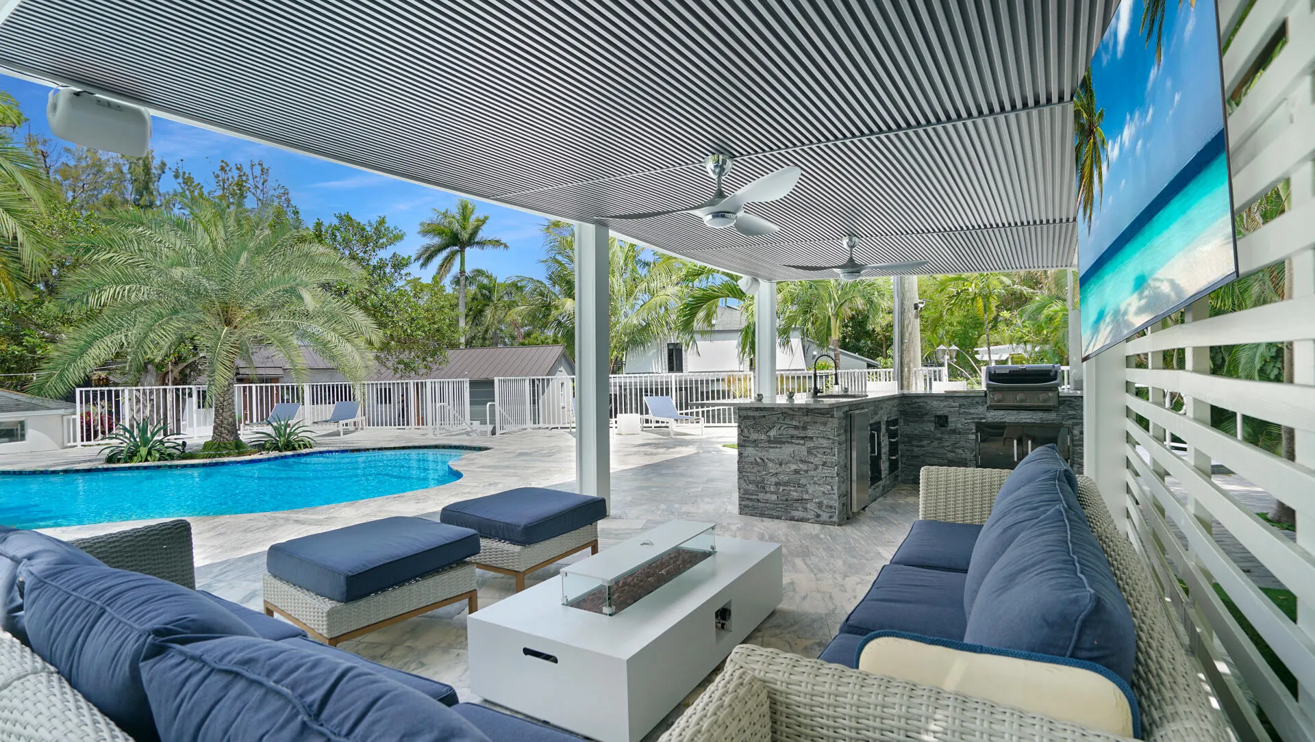 Covered patio featuring an outdoor kitchen with stone-finish cabinetry and built-in grill, dual ceiling fans, and a large flat-screen display
