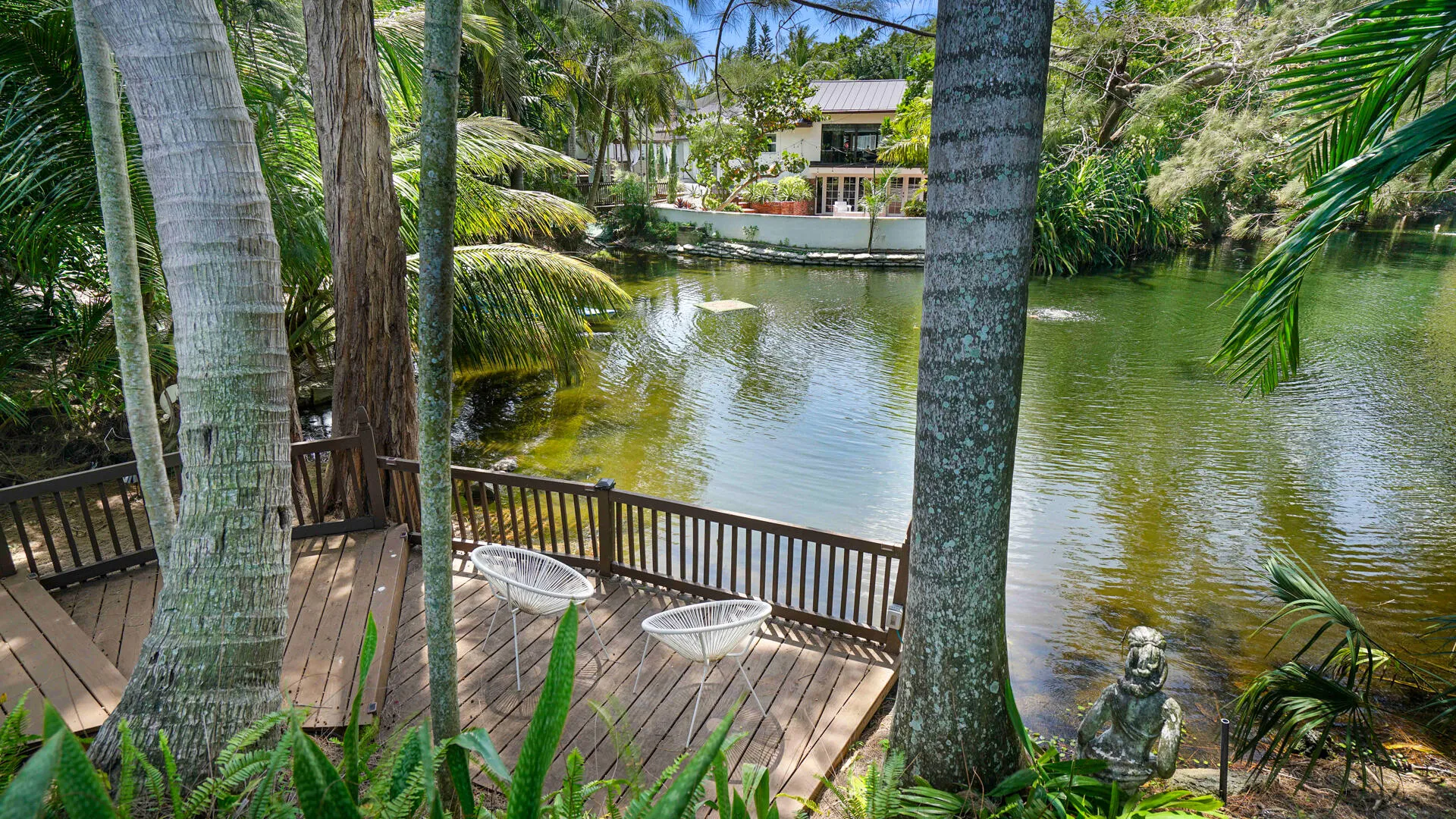 Expansive wooden deck with dark railing and verdant tropical landscaping overlooking a serene water feature