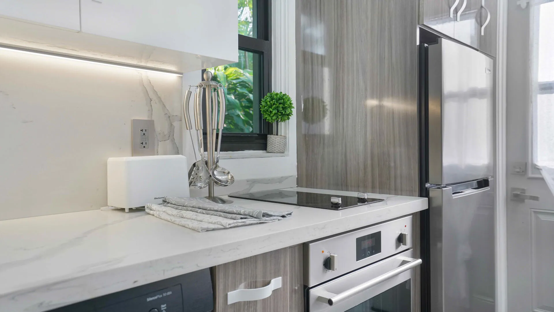 Kitchen featuring marble-patterned countertops, a built-in oven with a stainless steel finish, a glass cooktop, and a stainless steel refrigerator