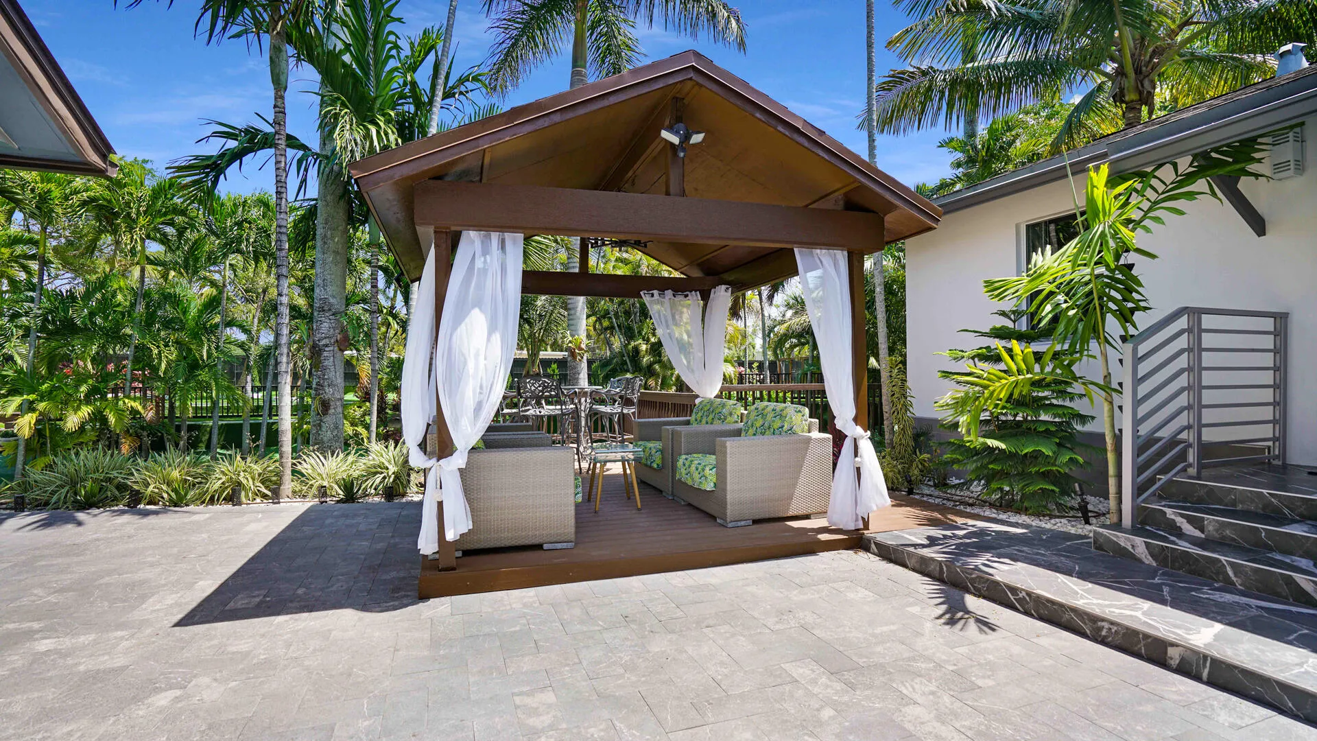Wood-finish gazebo with a pitched roof and sheer white curtains, set on a raised deck