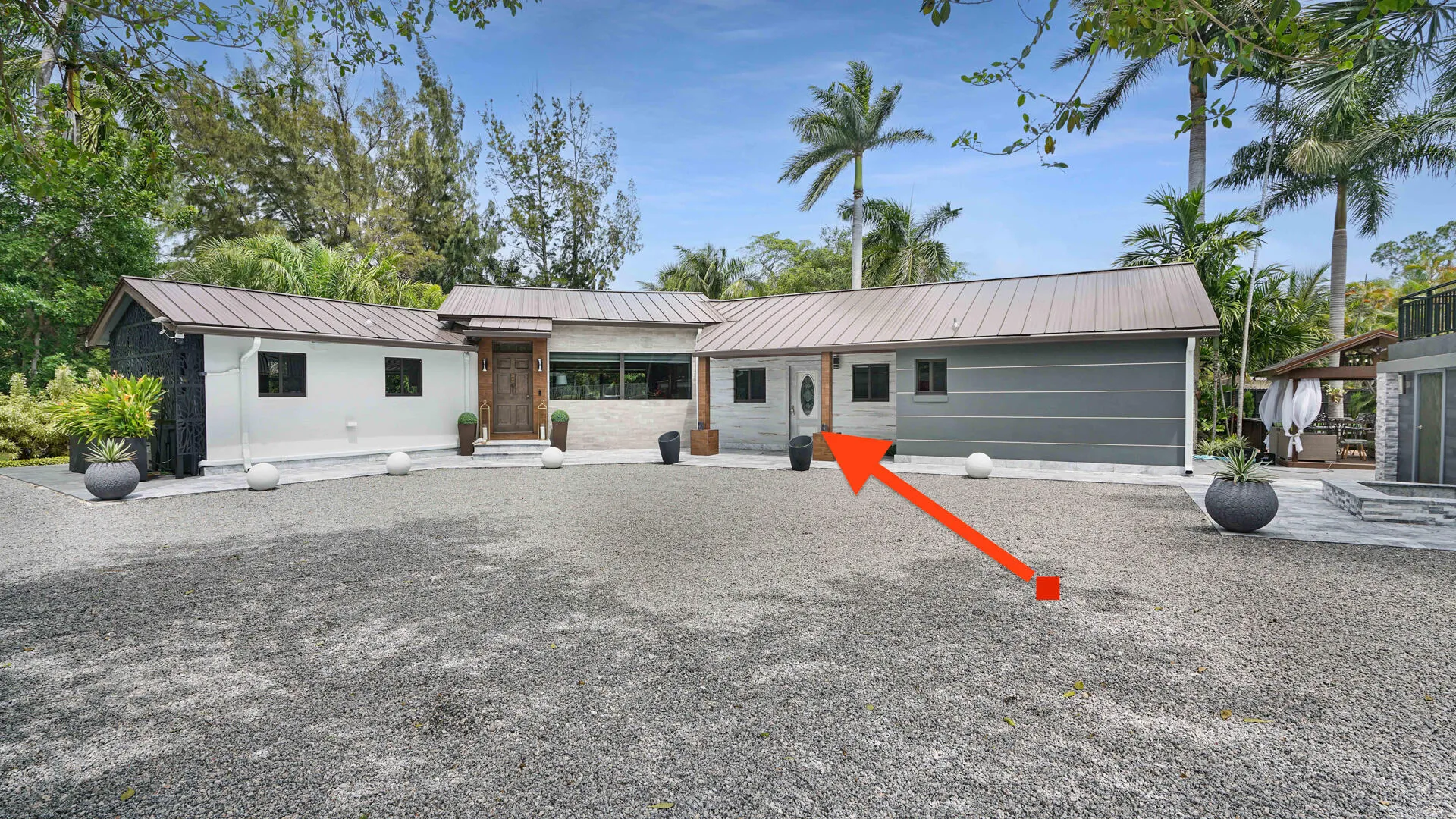 Contemporary exterior featuring a metal roof, white stucco, and dark siding with a gravel driveway