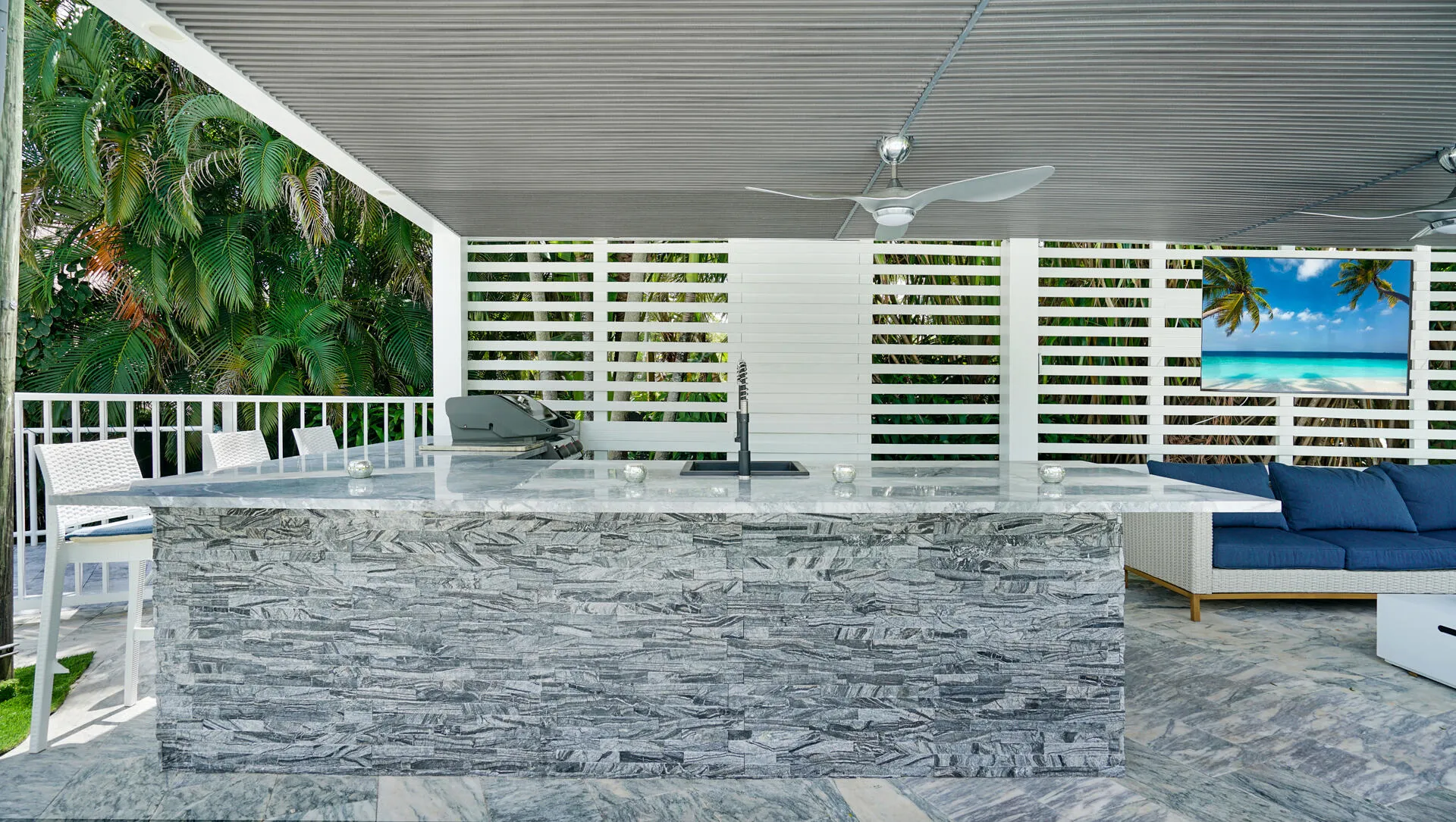 Outdoor kitchen featuring a stone-clad island with a light-toned countertop, integrated sink, and stainless steel grill