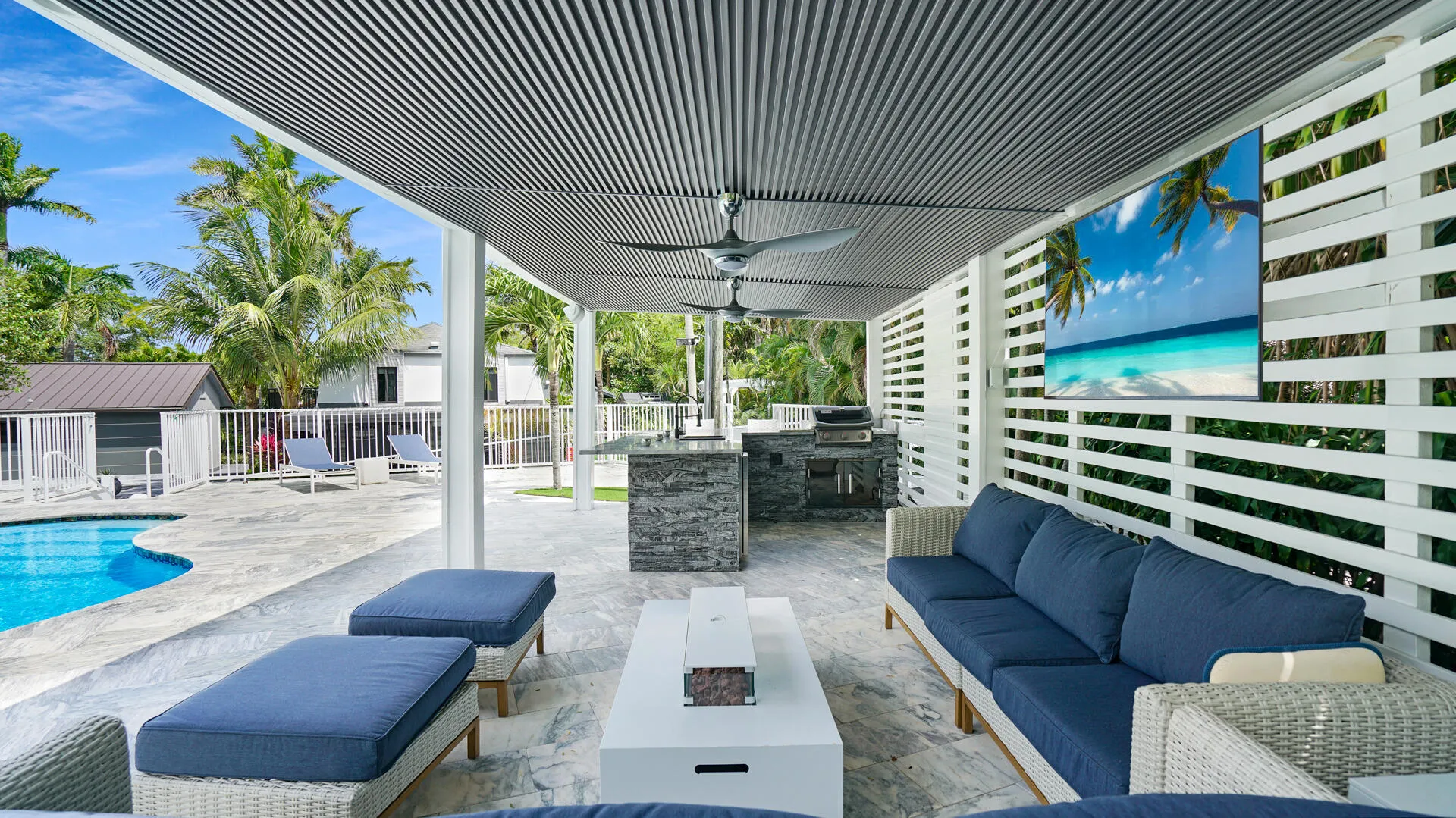 Covered outdoor patio featuring a slatted ceiling, built-in outdoor kitchen with stone veneer base, and a paved pool deck with a fenced swimming pool