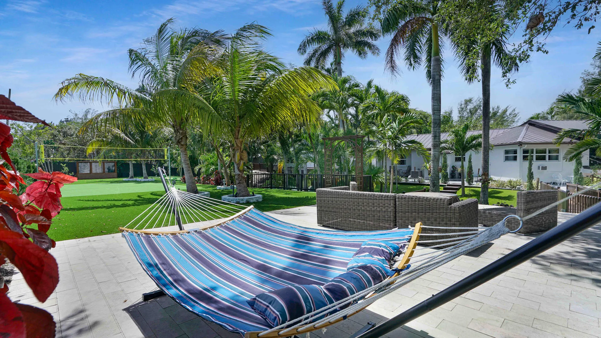 Expansive paver patio with tropical landscaping, artificial turf activity court, and mature palm trees