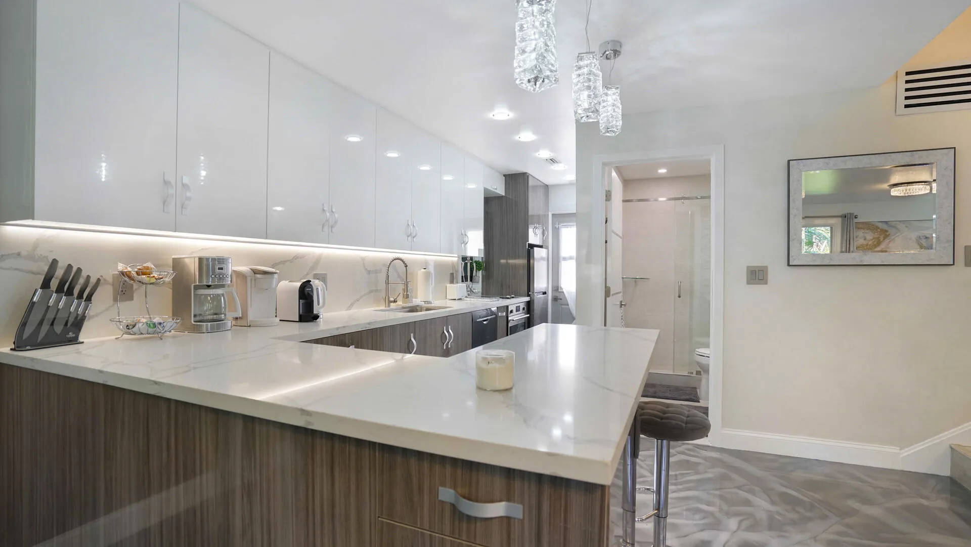 Modern kitchen featuring white high-gloss upper cabinetry, wood-finish lower cabinetry, and light-toned countertops with integrated lighting