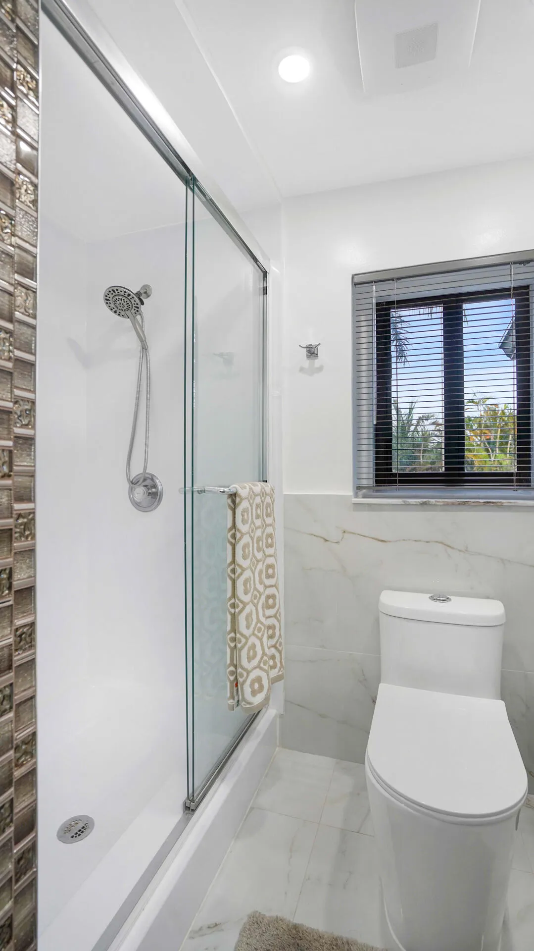 Walk-in shower with clear glass sliding door and mosaic tile accent wall