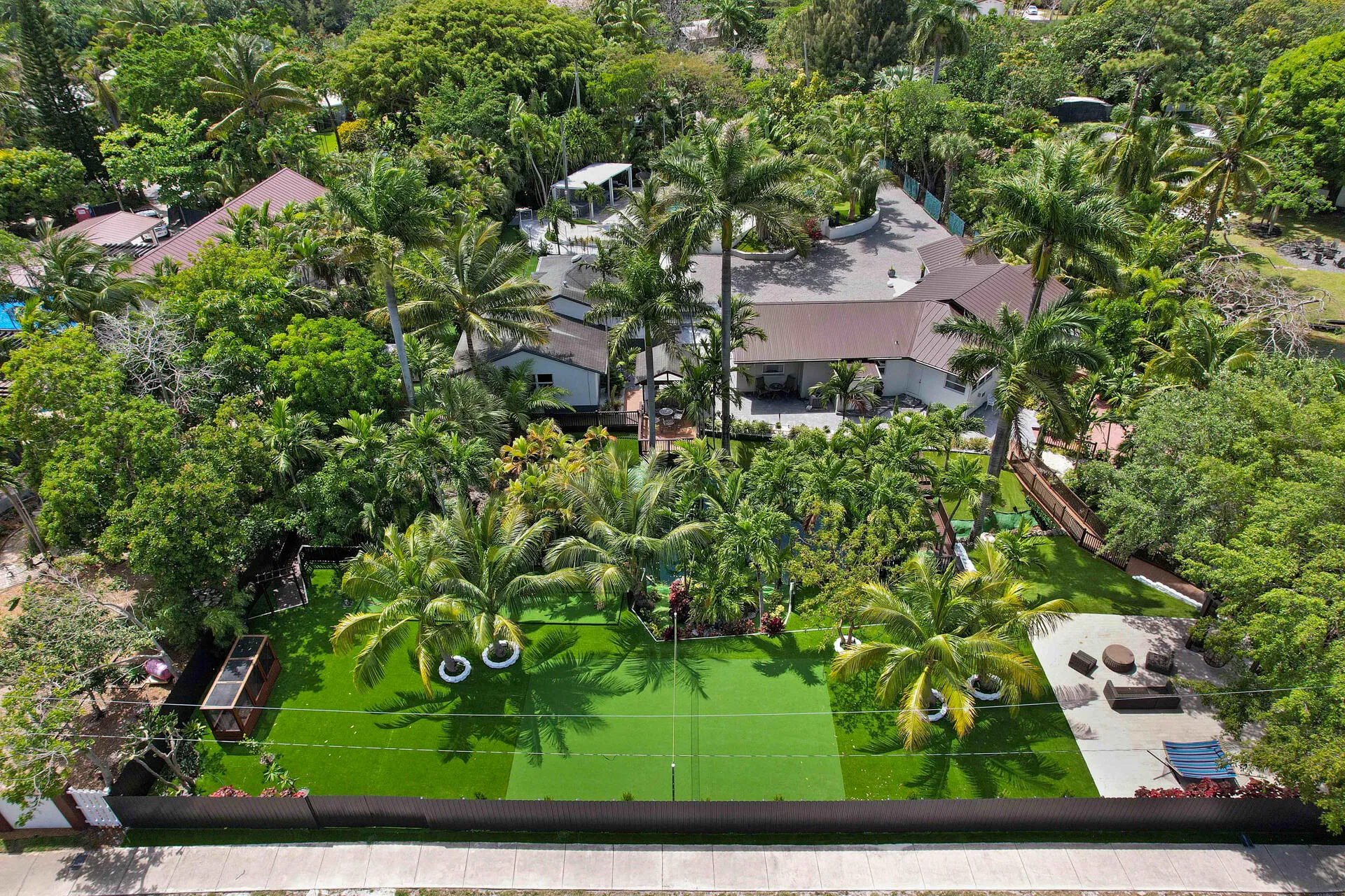 Spacious outdoor area featuring a synthetic turf court, mature palm trees, and an open patio