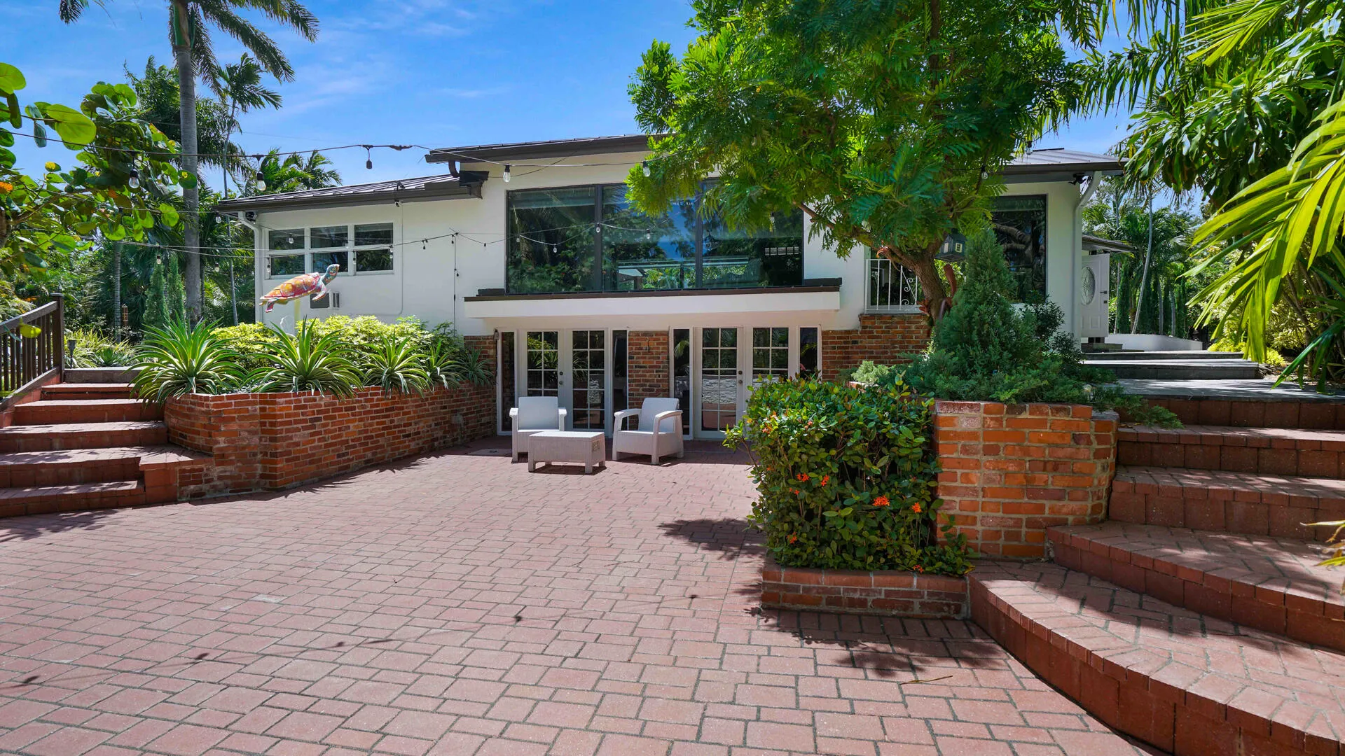 Spacious paver patio with a white exterior structure, large windows, and multiple entry points