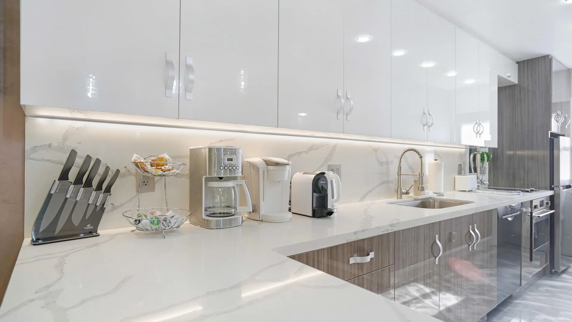 Modern kitchen featuring high-gloss white upper cabinetry, wood-finish lower cabinetry, and expansive light-toned countertops