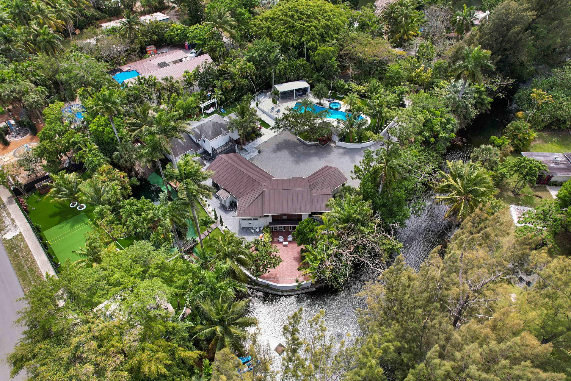 Expansive property featuring a multi-wing residence with a terracotta tile roof, a large swimming pool with integrated spa, a waterfront patio, and a dedicated artificial turf area