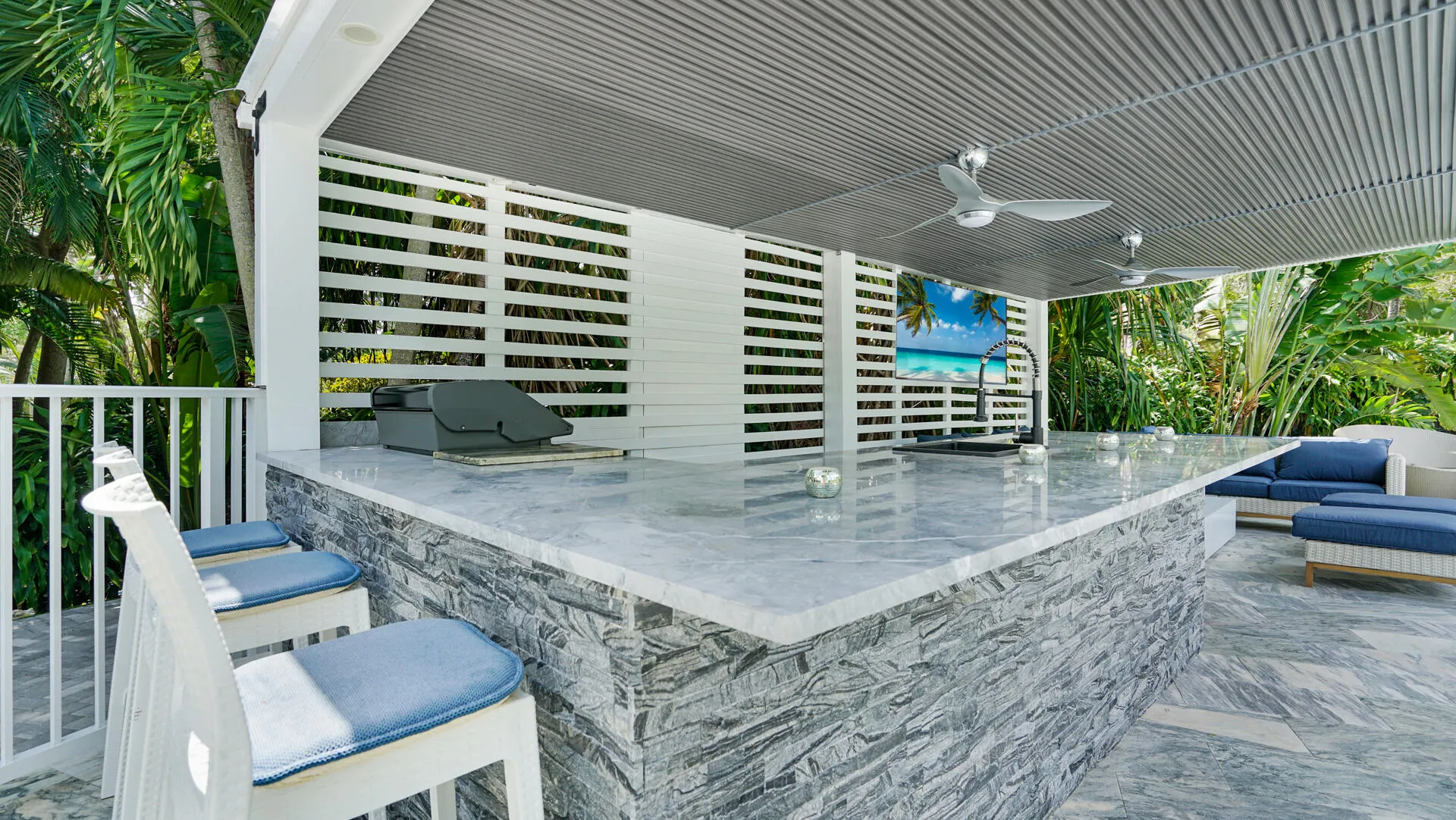 Outdoor kitchen featuring a stone-clad island, expansive countertop, built-in grill, and mounted sink with faucet