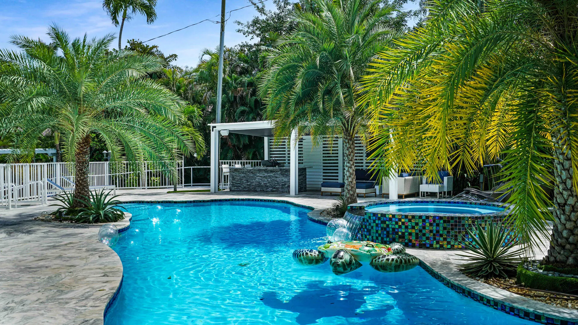 Freeform swimming pool with integrated spa featuring mosaic tile, surrounded by palm trees and stamped concrete decking