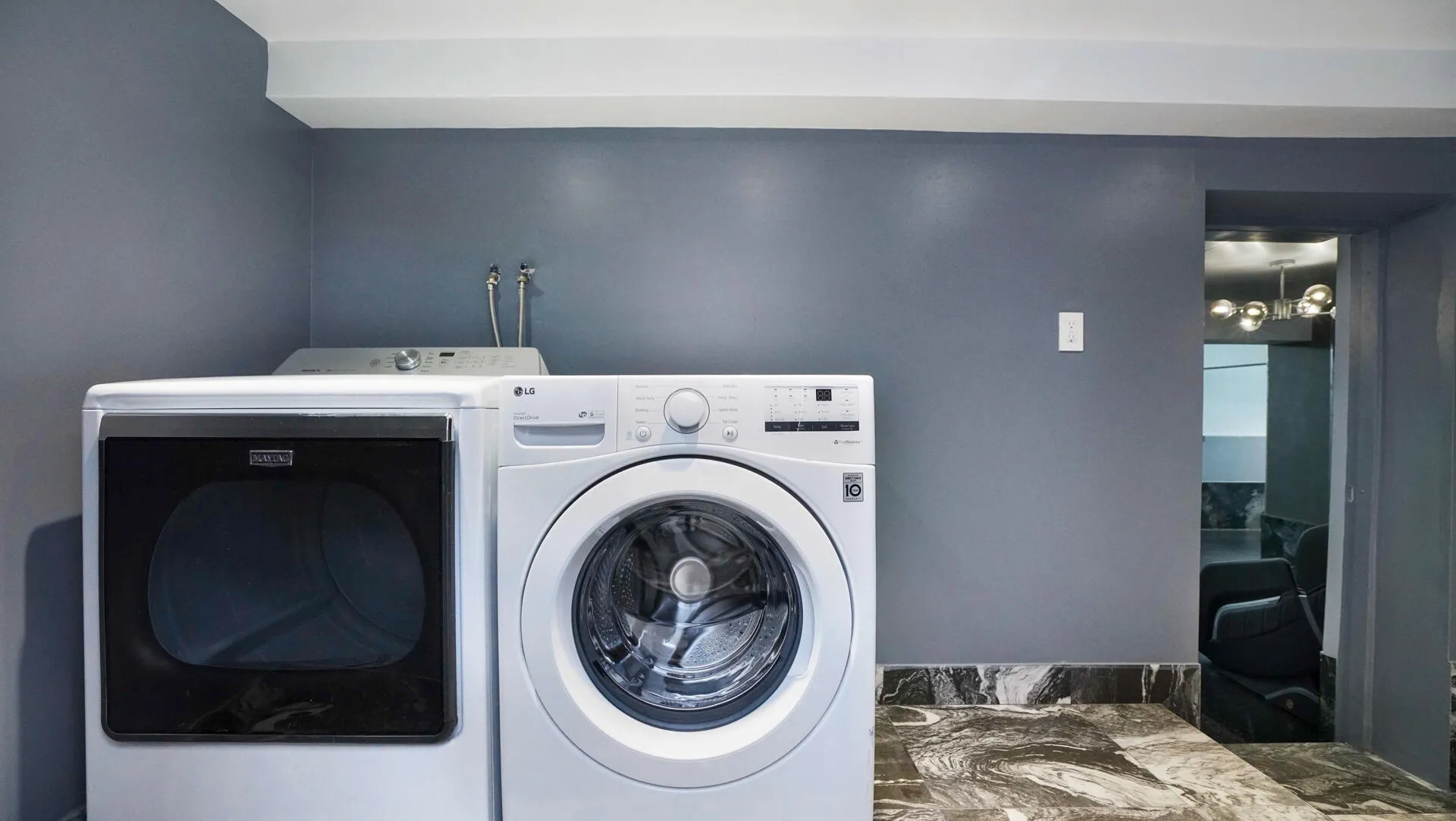 Laundry area featuring a front-loading washer and dryer, dark gray walls, and dark patterned floor tiles