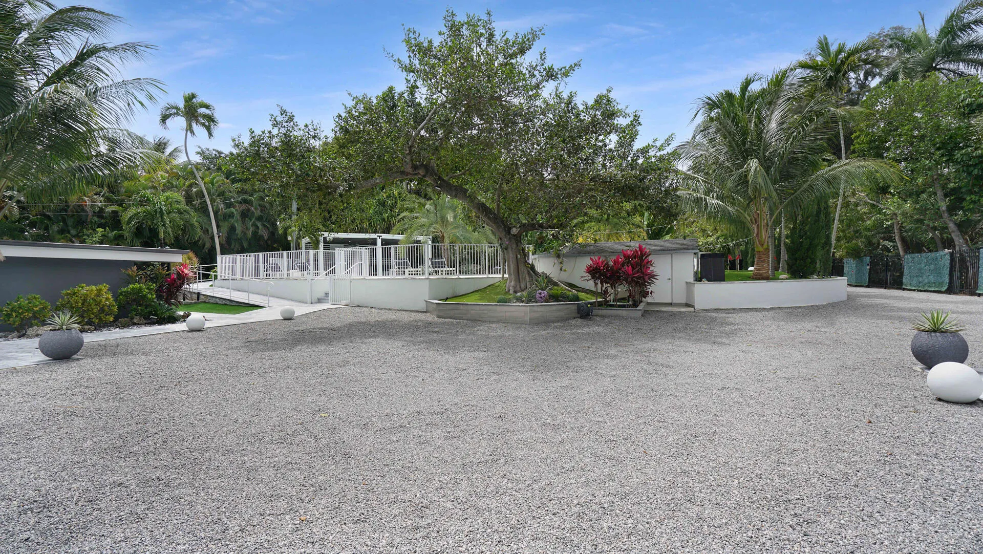 Expansive gravel driveway with tropical landscaping and mature trees