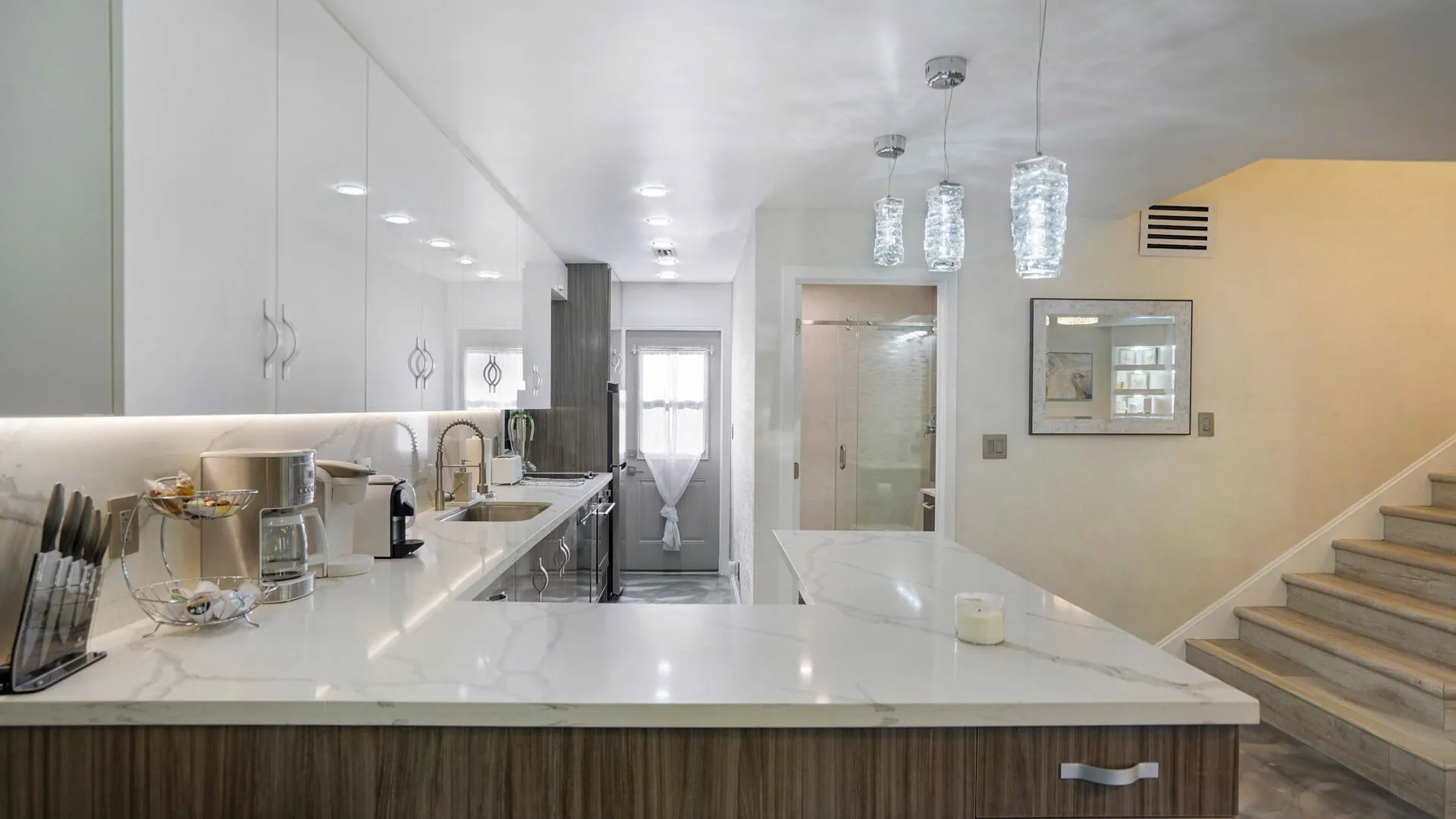 Modern kitchen featuring a white countertop with subtle veining, wood-finish base cabinetry, white upper cabinetry, and recessed lighting