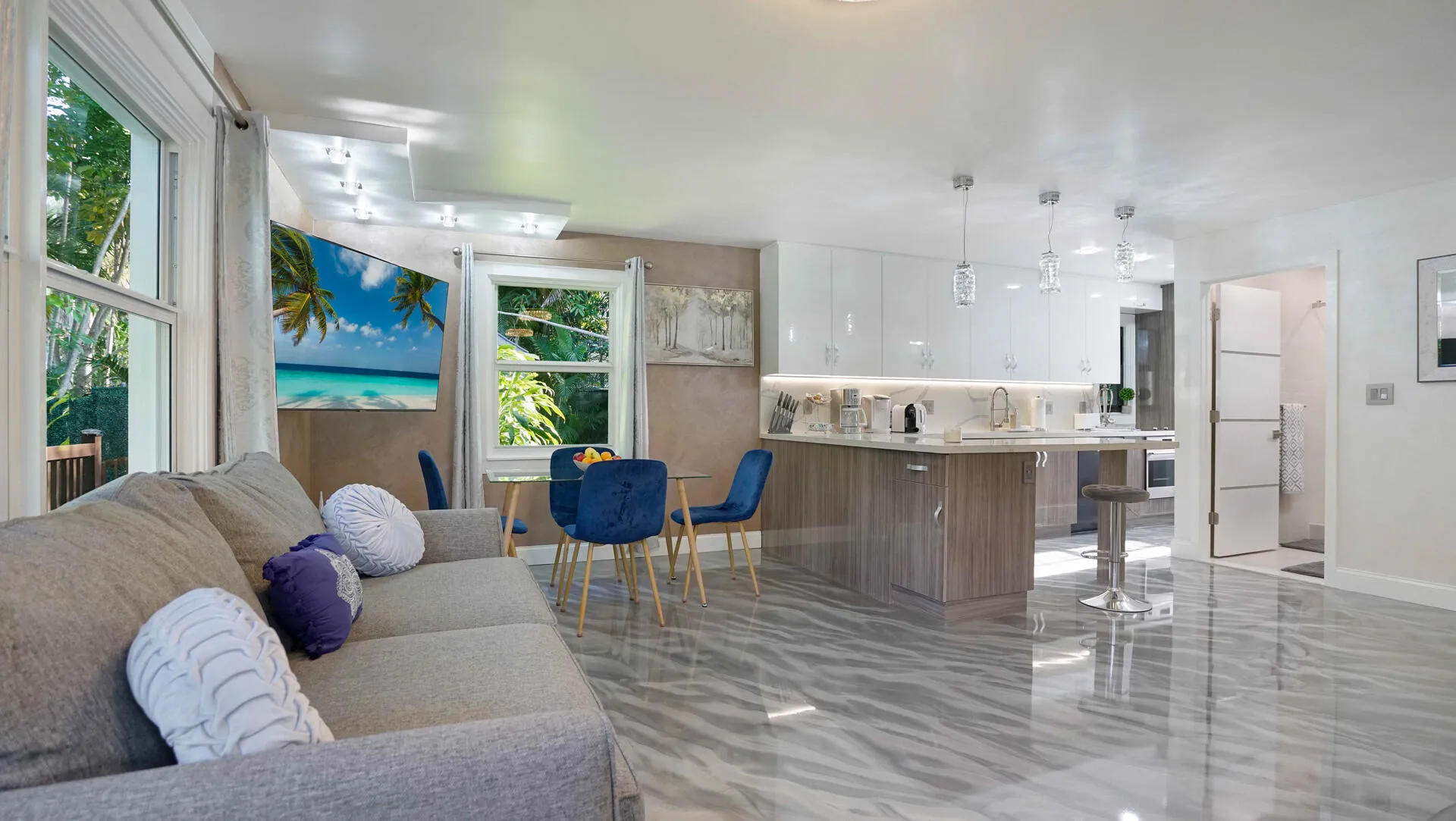 Open-concept living area featuring a modern kitchen with high-gloss white cabinetry, a large island with wood-finish paneling, and an integrated sink