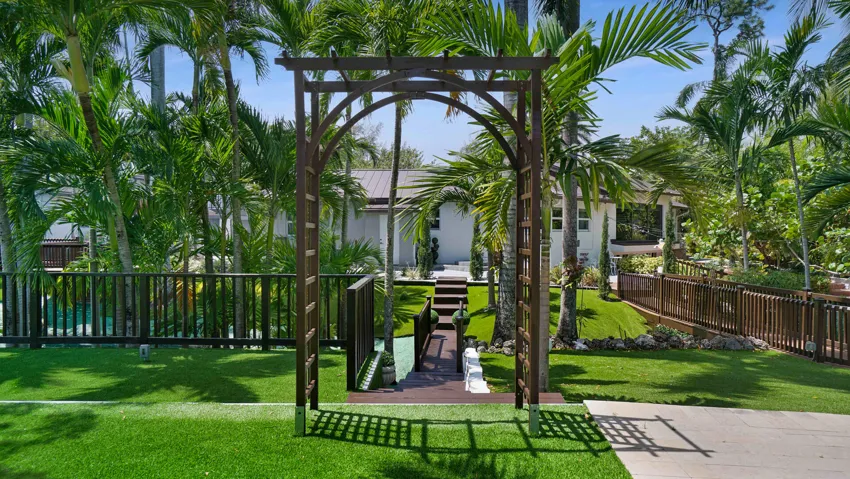 Landscaped exterior featuring a decorative wooden archway, lush green lawn, and mature palm trees