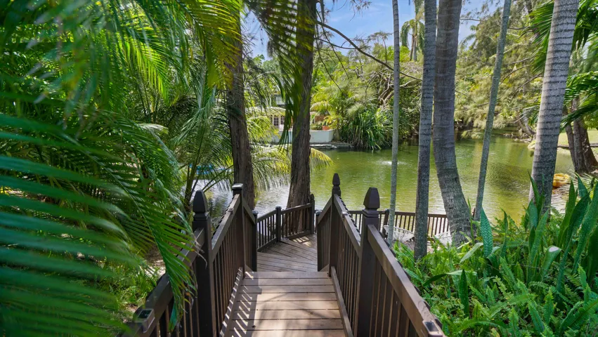 Expansive wood-finish deck with dark railings leading to a tranquil pond