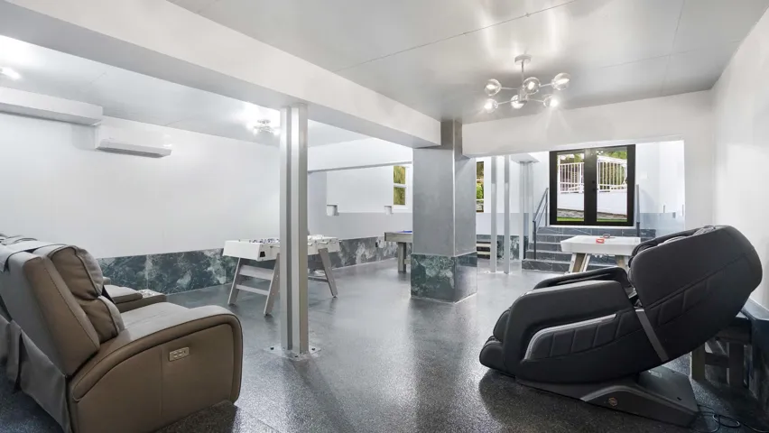 Spacious recreational area featuring polished concrete flooring, a modern multi-bulb light fixture, white walls, and a dark marble-look wainscoting