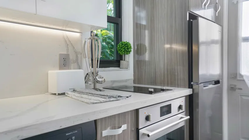 Kitchen featuring marble-patterned countertops, a built-in oven with a stainless steel finish, a glass cooktop, and a stainless steel refrigerator