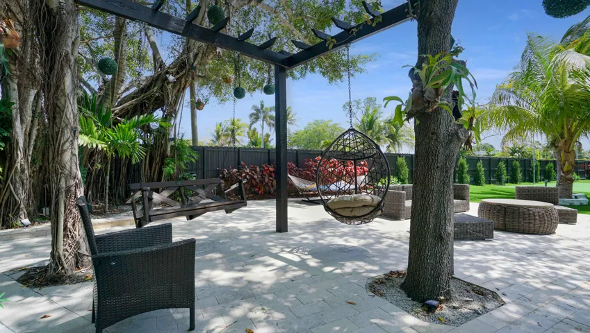 Expansive outdoor patio featuring light-toned paver flooring, a dark-stained wood pergola, and mature trees