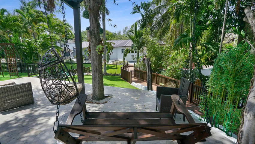 Outdoor patio area featuring paver flooring, mature tropical landscaping, and a wooden bridge