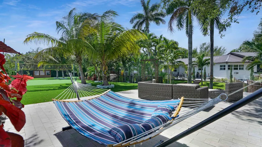 Expansive paver patio with tropical landscaping, artificial turf activity court, and mature palm trees