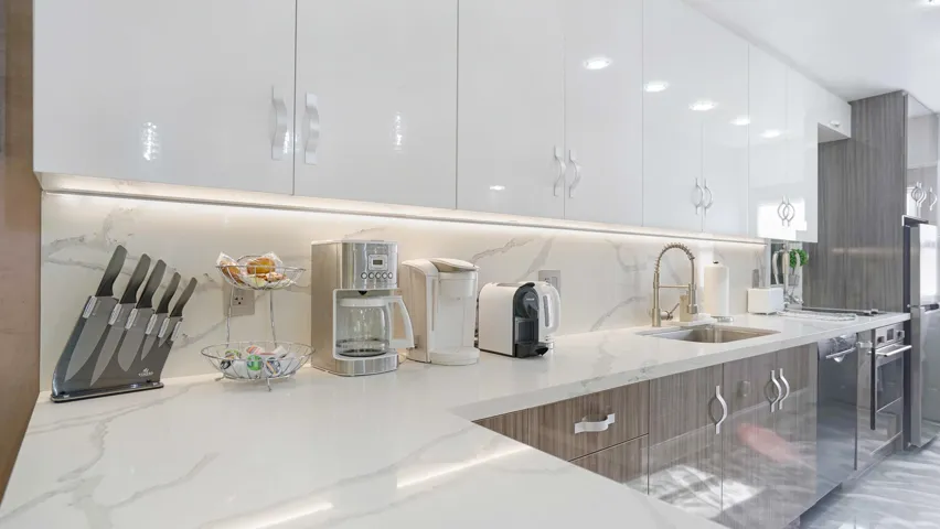 Modern kitchen featuring high-gloss white upper cabinetry, wood-finish lower cabinetry, and expansive light-toned countertops