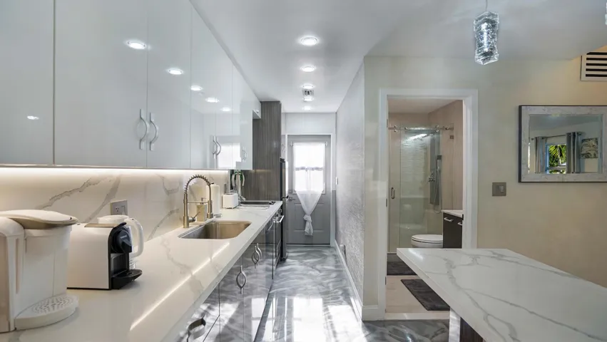 Galley kitchen featuring high-gloss white upper cabinetry, under-cabinet lighting, and a coordinating stone-finish countertop with integrated sink