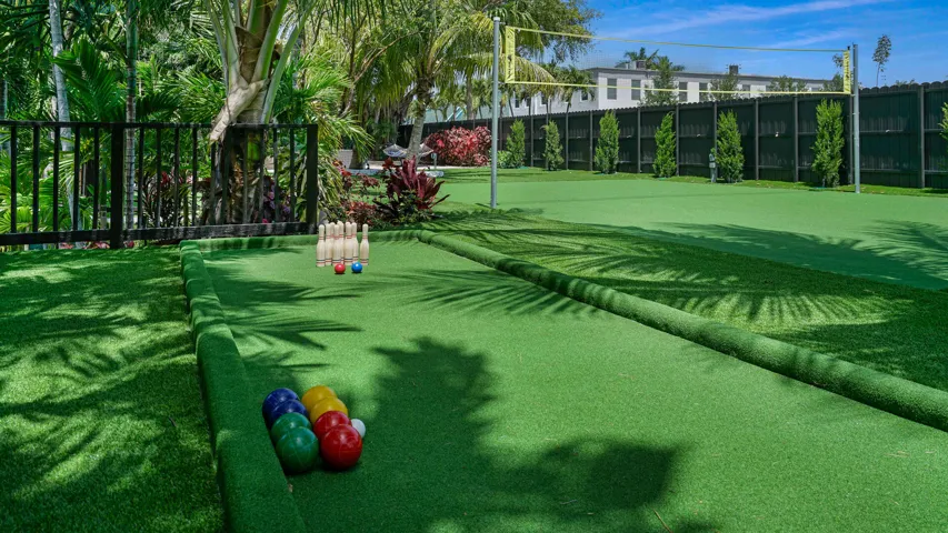 Expansive artificial turf area featuring a dedicated bowling lane, a volleyball court with net, and lush tropical landscaping