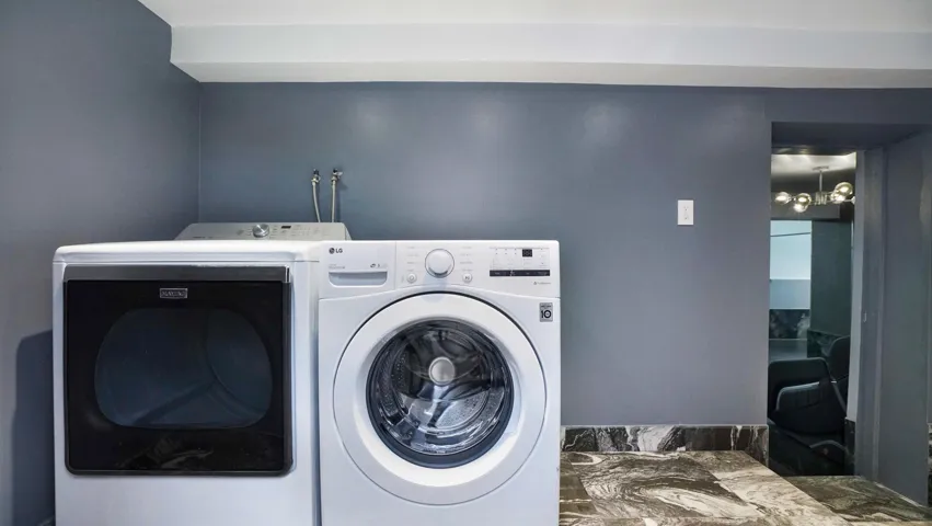 Laundry area featuring a front-loading washer and dryer, dark gray walls, and dark patterned floor tiles
