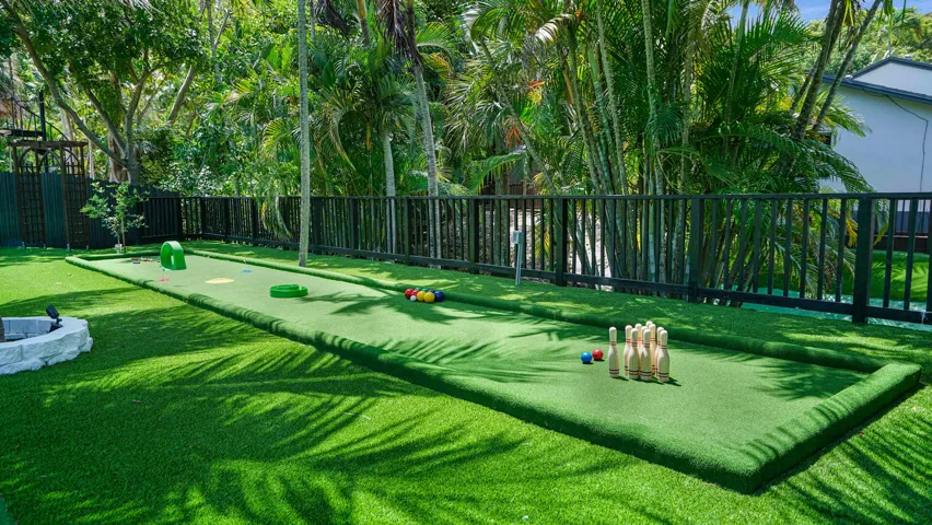 Expansive turf backyard featuring a putting green, a dark-toned fence, and mature tropical landscaping